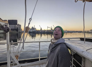 Brad Vogel smiling in winter hat and scarf aboard boat on water at sunrise